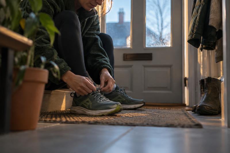 Hands tying running shoes beside a front door at dawn